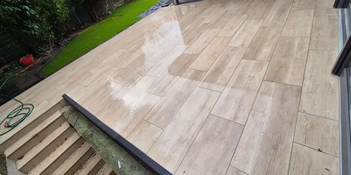 Fertige Terrasse mit Fliesen in Holzoptik, angrenzend an Rasenfläche und Treppe