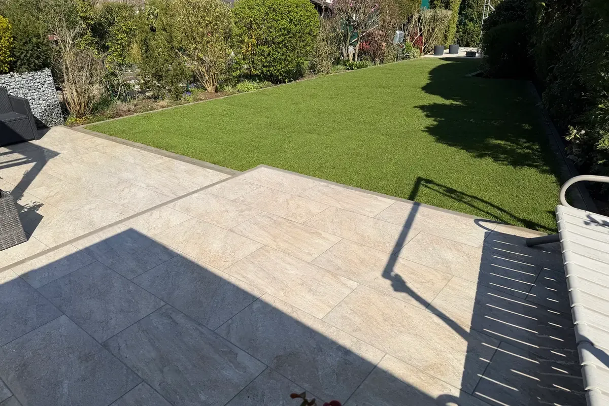 Fertige Terrasse aus grauen und beigen Großformatplatten mit angrenzender Rasenfläche, gebaut von BALA Gartenbau & Fliesen in Viersen