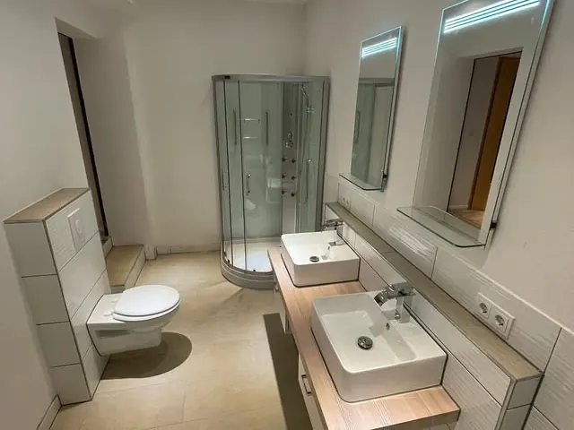 Dasselbe Badezimmer aus anderer Blickrichtung, mit Doppelwaschtisch auf Holzkonsole und gefliestem Spiegelbereich