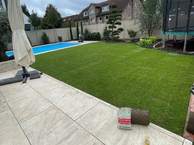 Angelegter Garten mit frisch verlegtem Rollrasen, Pool und heller Terrasse aus Großformatplatten