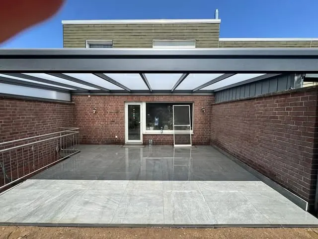 Dieselbe Terrasse nach der Sanierung mit grauen Großformatplatten und Terrassenüberdachung