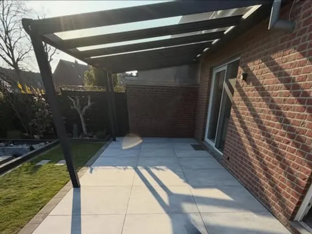 Terrassenüberdachung mit Glasdach an einer Klinkerfassade über hellgrauen Großformatplatten